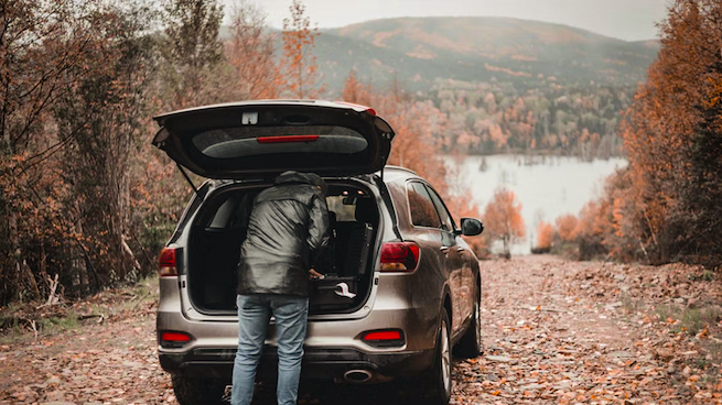 Man unloading camera equipment from his car with beautiful fall colors in the background