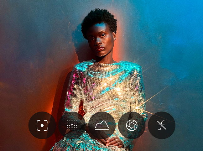 Demonstration of Pro controls UI menu, Camera app, controls for lens aperture, shutter speed, white balance, and histogram displayed, overlaid on a picture of person wearing a sparkly metallic dress against a colorful backdrop