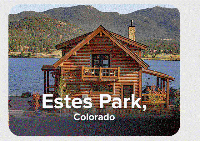 Log cabin with lake views, mountain backdrop, and surrounding evergreen trees.