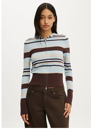 Woman wearing a striped cropped cardigan with blue, cream, and brown stripes with brown ribbed pants
