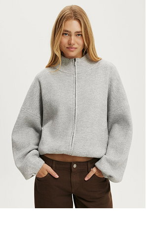 Woman wearing a light grey zip-up cropped sweater and brown pants