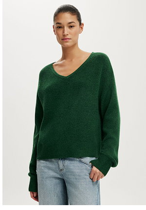 Woman wearing a dark green v-neck sweater with long sleeves and light blue jeans