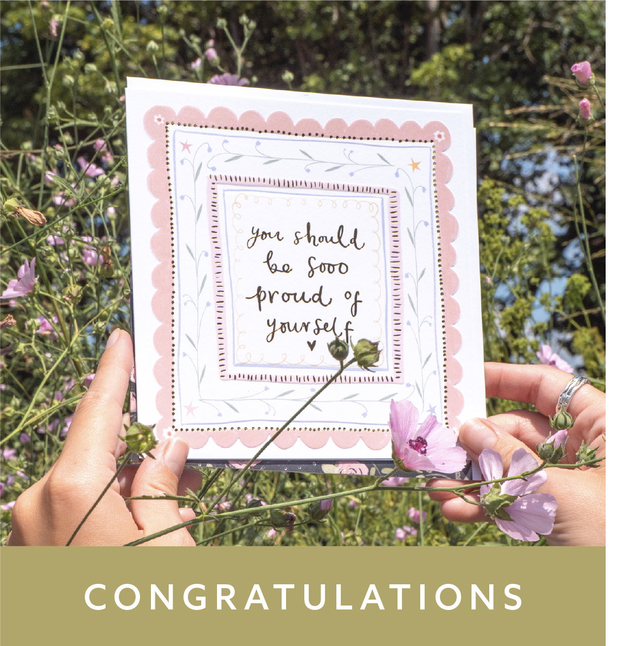 Congratulations card with a pink scalloped border, held amongst garden flowers. Shop Congratulations cards.
