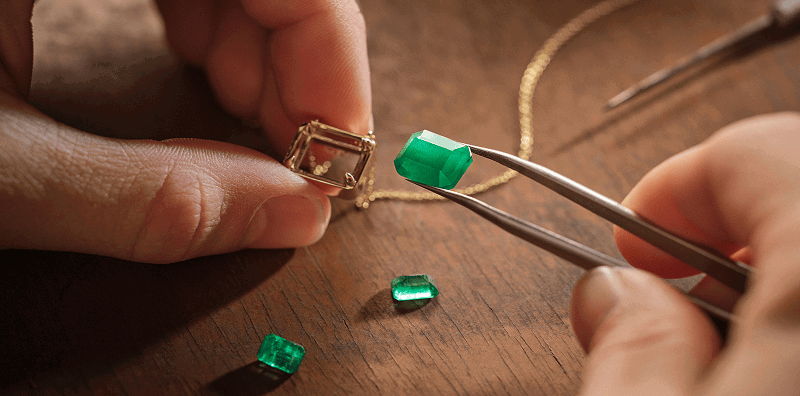 Two hands repairing an emerald pendant necklace. 