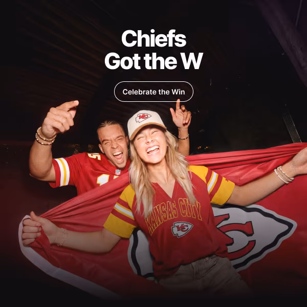 Two fans celebrate a victory. The person in front holds out a team flag across their back.