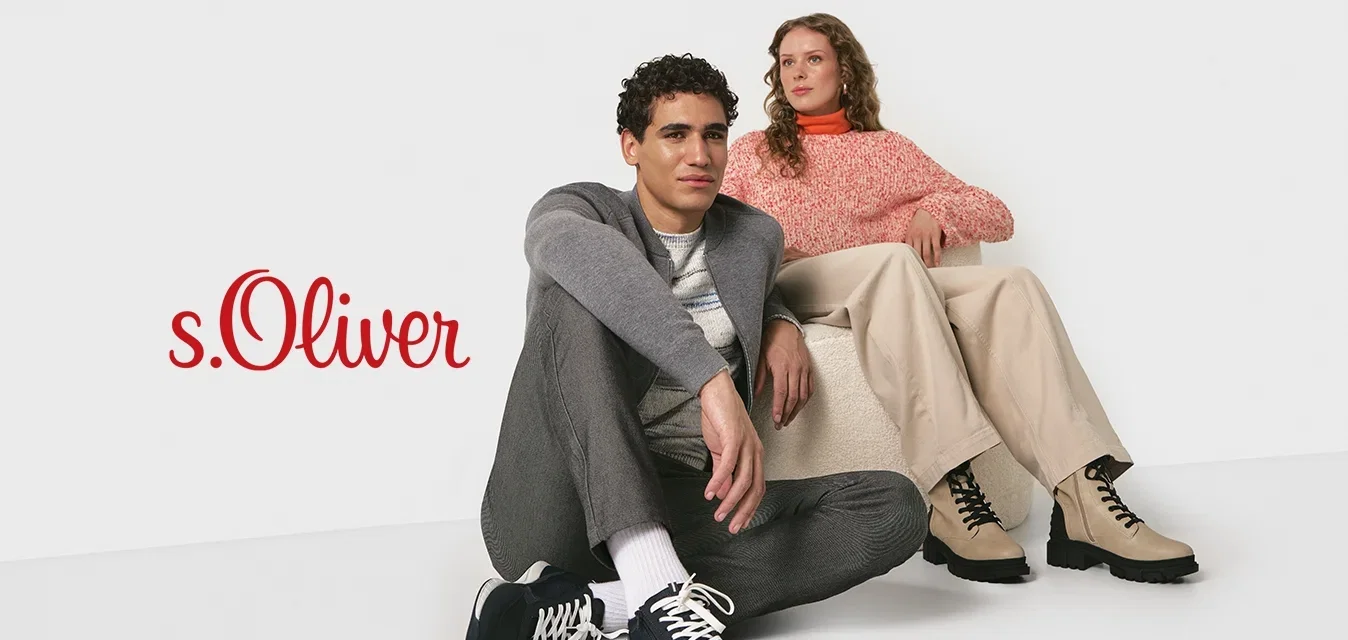 Twee jonge volwassenen in casual herfstoutfits; de één zit op de vloer in sneakers, de ander op een lage stoel met beige laarzen tegen een witte achtergrond.