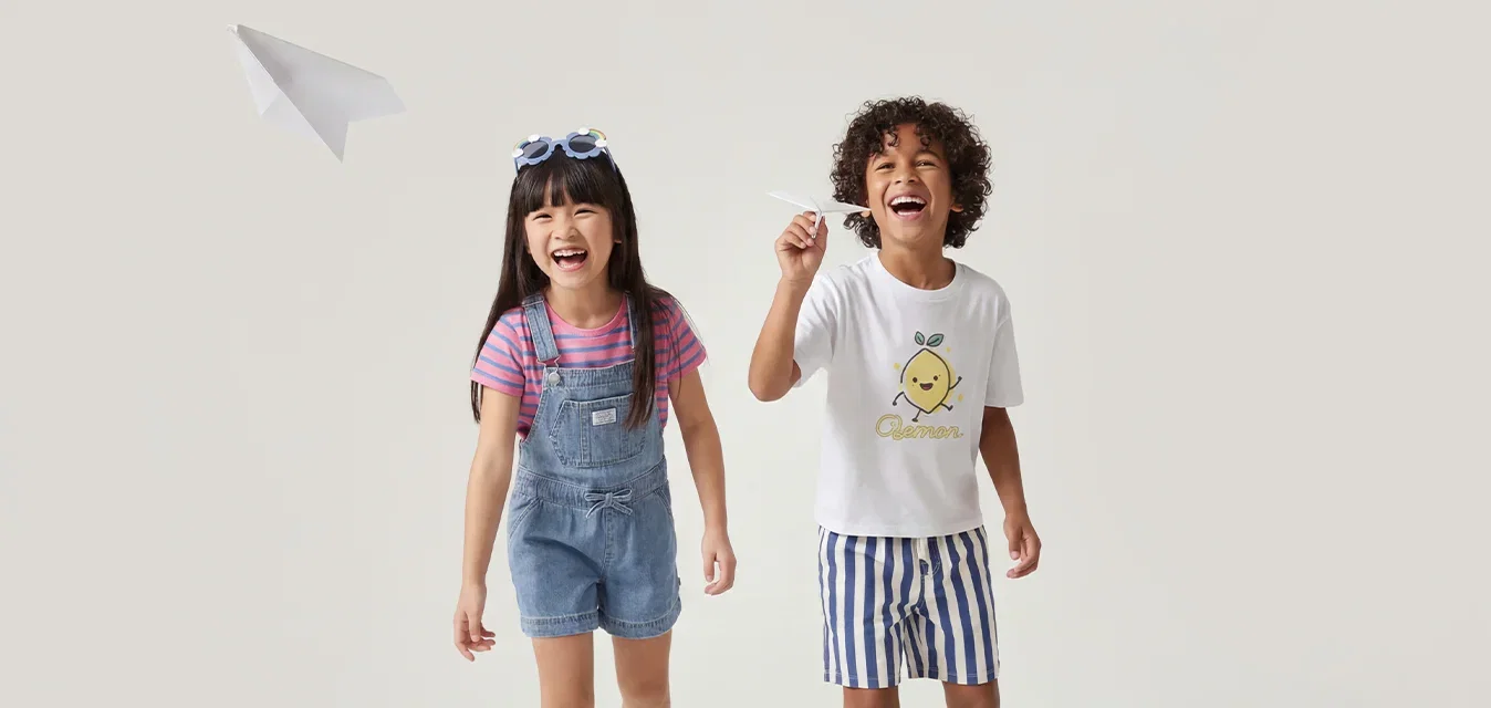Twee kinderen lopen en lachen, waarbij een jongen een papieren vliegtuigje tegen een effen lichte achtergrond gooit.