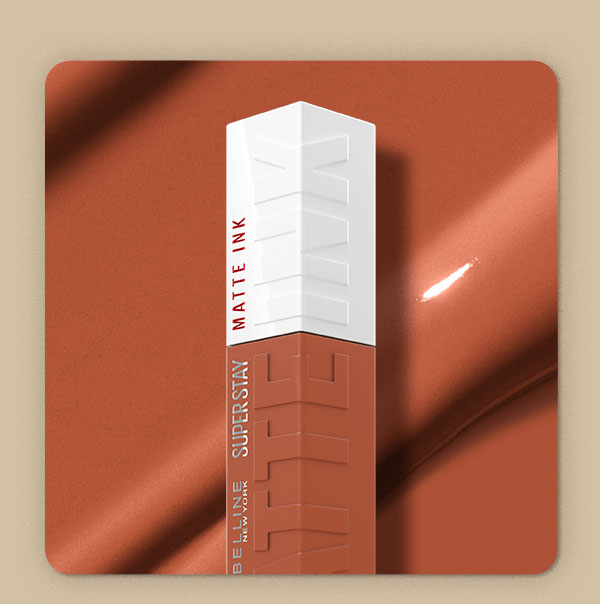 Top of a Maybelline Super Stay Matte Ink Liquid Lipstick bottle in Amazonian, a warm caramel-brown shade, set against a copper satin backdrop with a swipe of glossy textured shade swatch.
