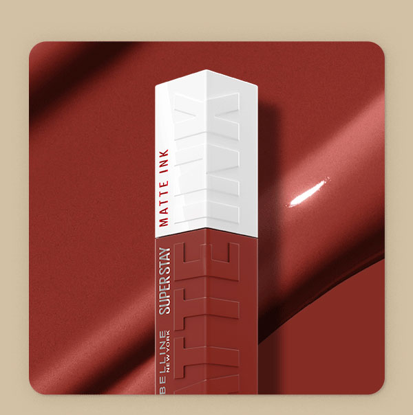 Top of a Maybelline Super Stay Matte Ink Liquid Lipstick bottle in Charmer, a warm terracotta-red shade, set against a rich rust satin backdrop with a swipe of glossy textured shade swatch.