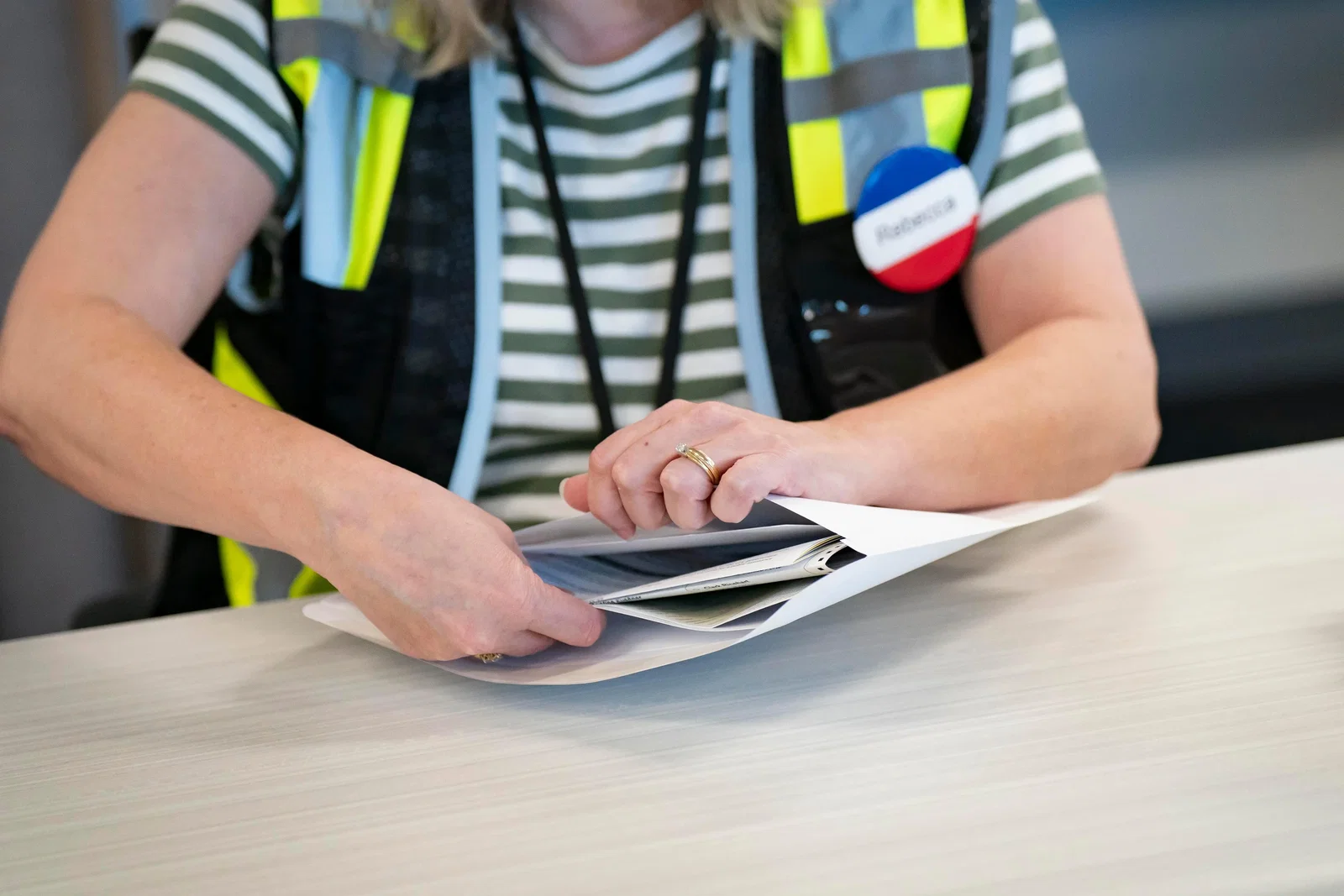 A worker in a vest and badge puts documents in a mailing envelope.