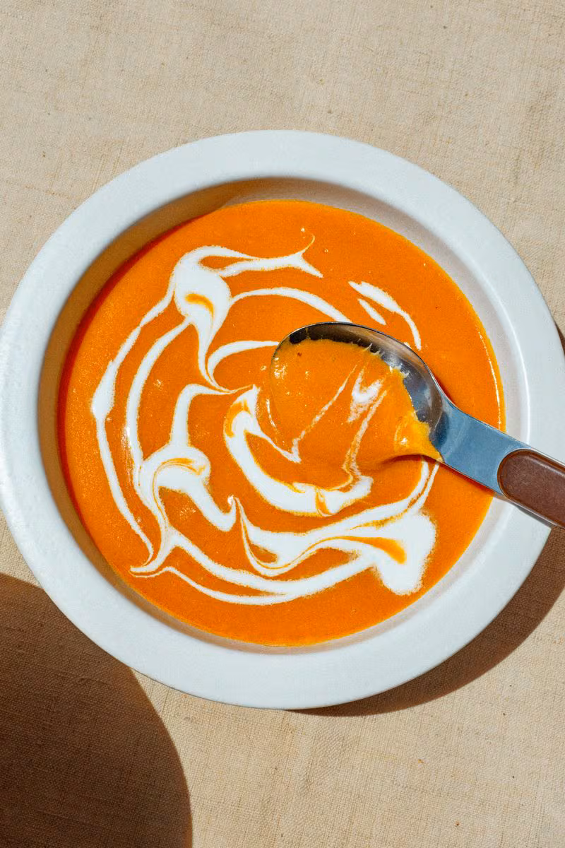 Pumpkin Curry soup in a white bowl with a spoon sweeping through