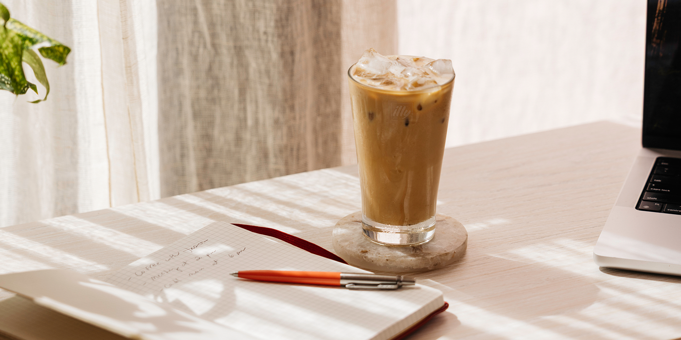 Iced coffee on a sunlit desk beside a notebook and laptop