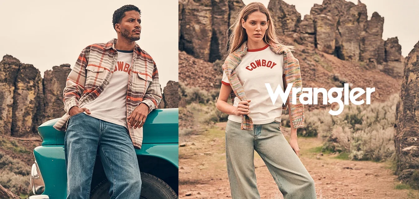 Een man leunt op een turquoise vintage vrachtwagen terwijl een vrouw vlakbij staat; beiden dragen casual kleding met een cowboythema in een rotsachtig woestijnlandschap.