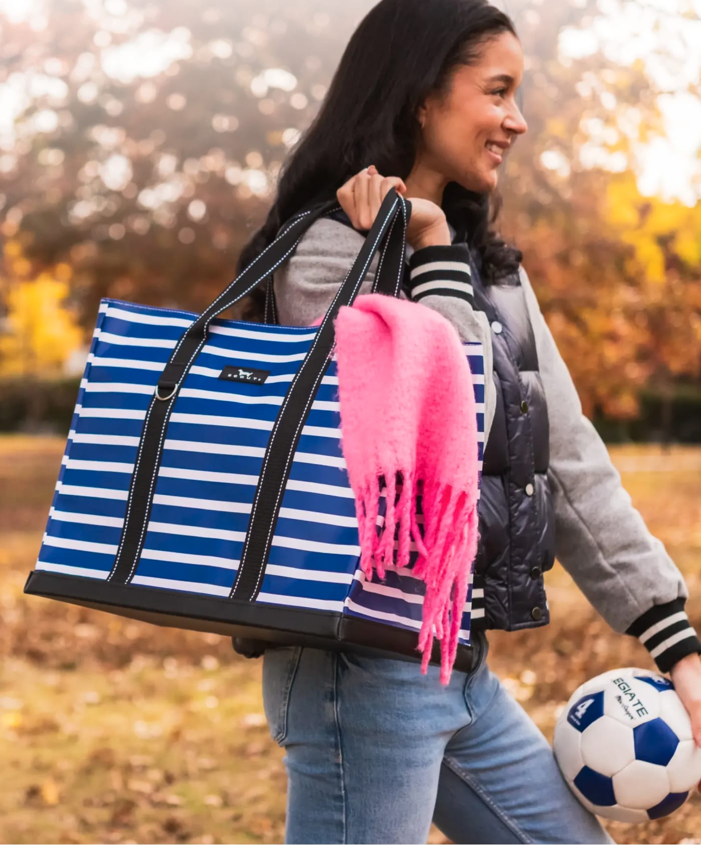 Woman carrying a blue and white striped SCOUT tote bag with a pink scarf and a soccer ball.