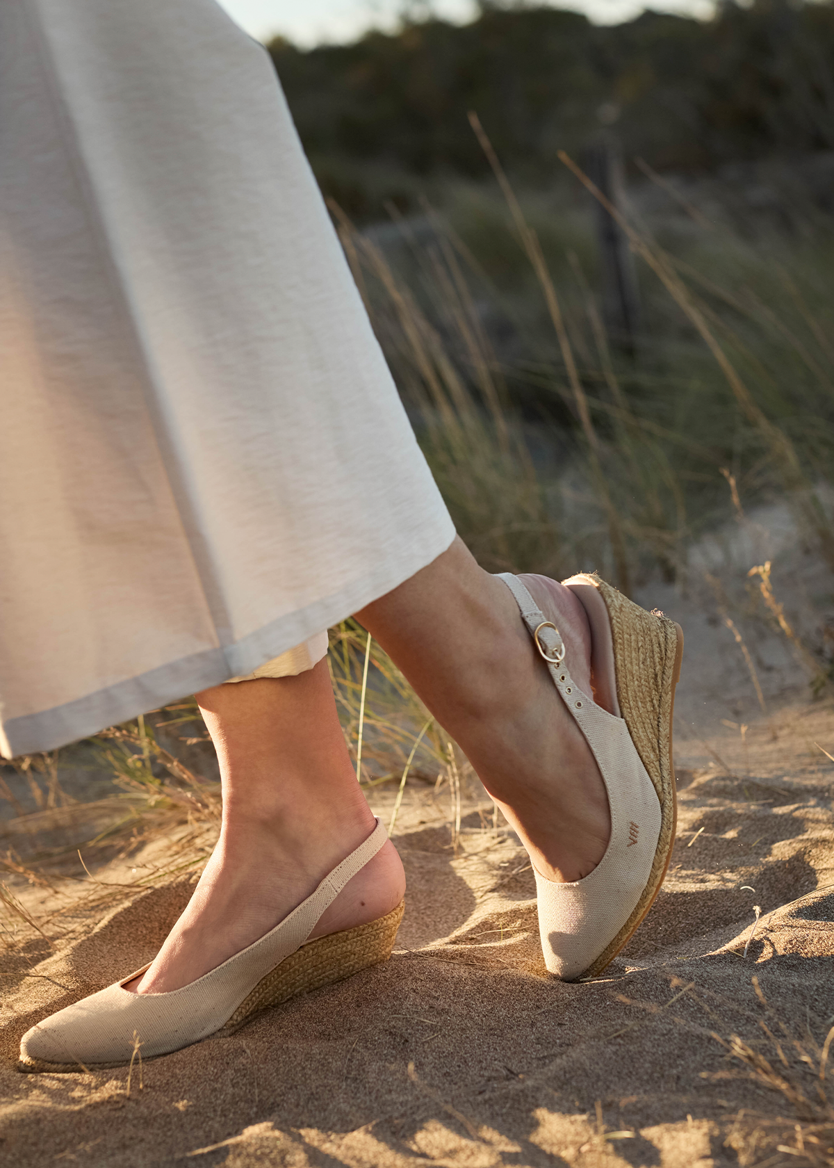Woman wearing beige Palomera canvas slingback wedge espadrilles by Viscata on sunlit beach sand.