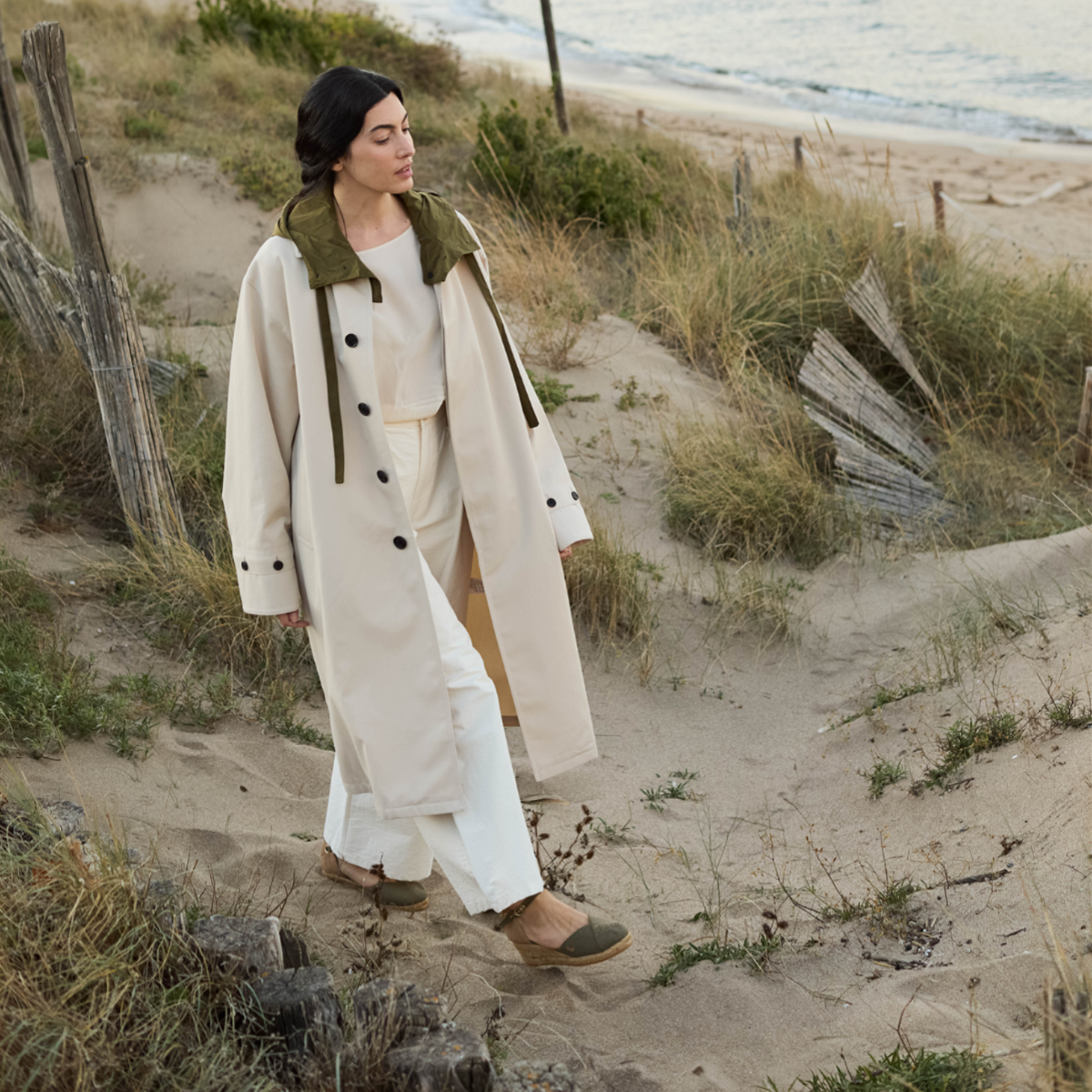 Woman wearing olive Pubol canvas ankle-strap wedge espadrilles by Viscata while walking through coastal sand dunes.