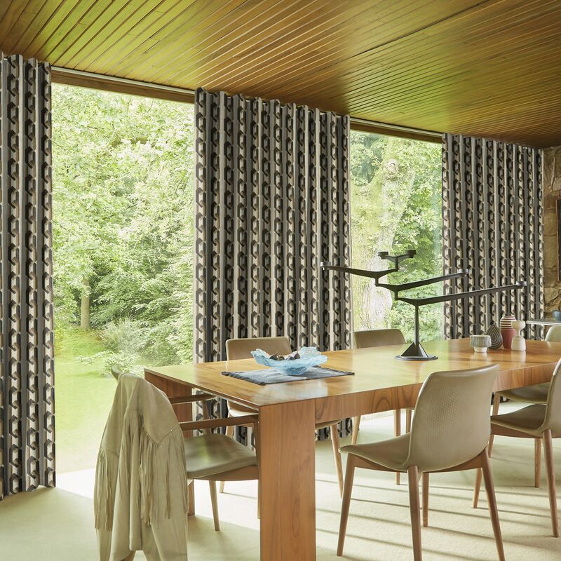 Floor-to-ceiling patterned curtains frame large windows, filling a stylish dining room with natural light and garden views.