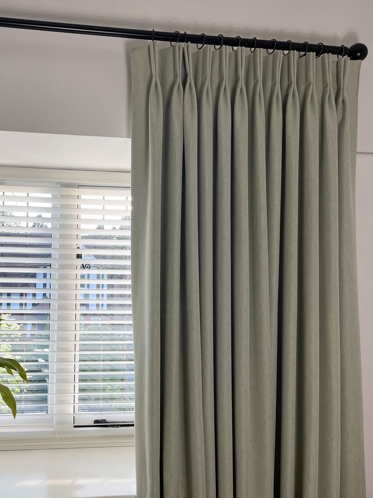 Pinch pleat curtain on a black pole pairs with wide white Venetian blinds, offering flexible light control and privacy at the window.
