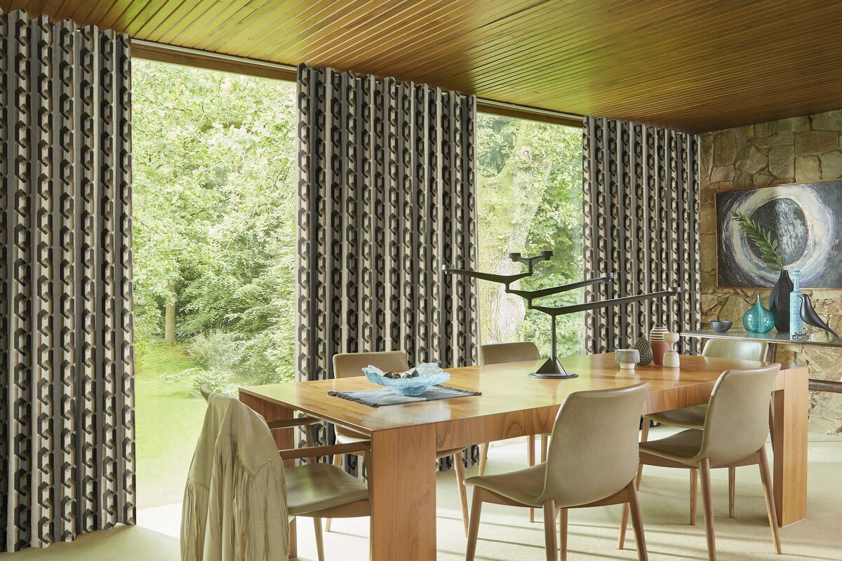 Floor-to-ceiling patterned curtains frame large windows, filling a stylish dining room with natural light and garden views.