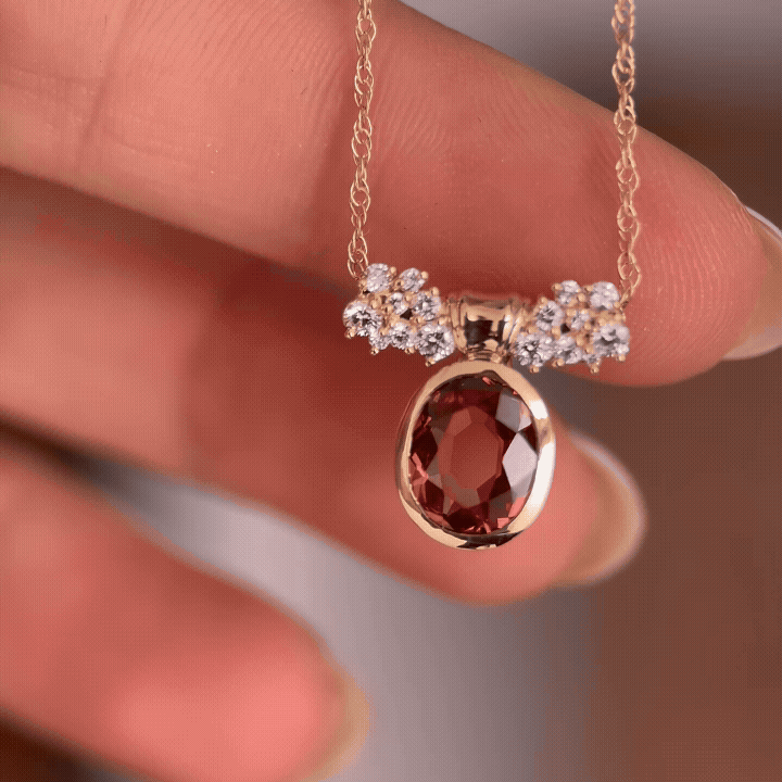 The Corridor Necklace in Malaya Garnet, 0.96ct Oval Cut shown dangling in front of a light brown background and placed into position by a model.