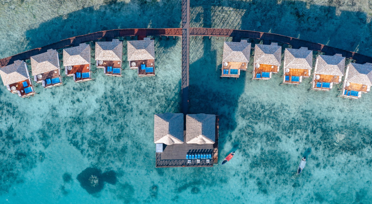 Aerial shot of overwater bungalows on a calm, turquoise sea at dusk.