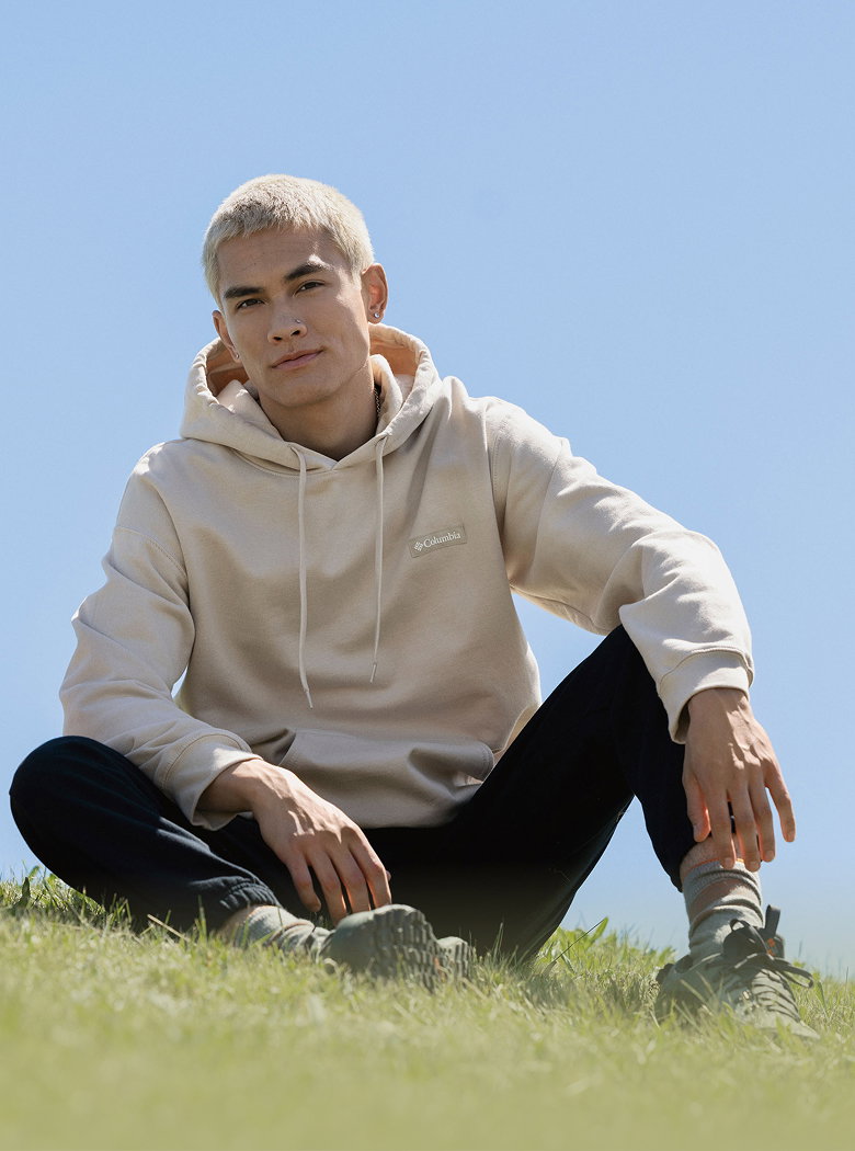 A man sitting in the grass wearing a white sweatshirt and black pants 