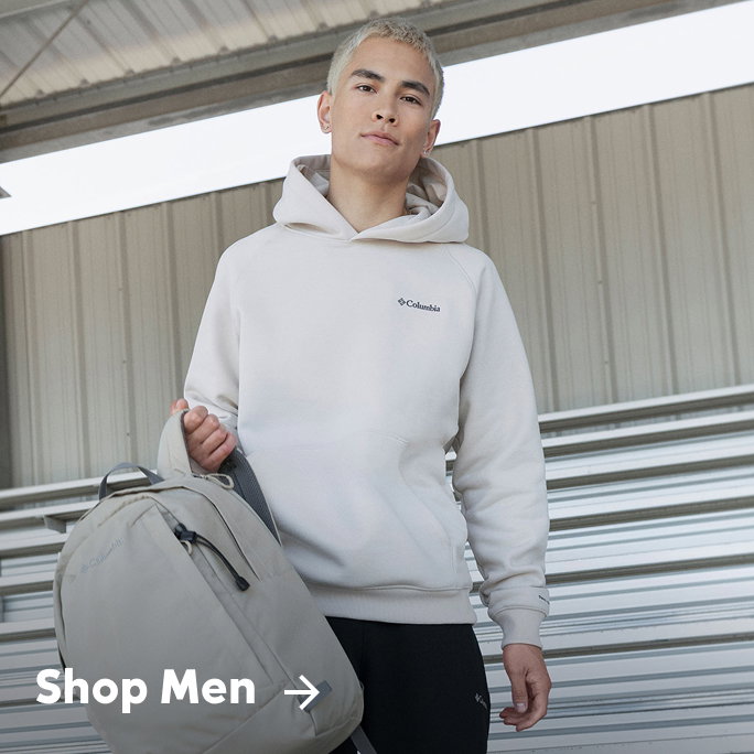 A man wearing a white sweatshirt, carrying a backpack on the bleachers with text: Shop Men