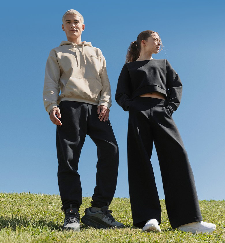 A man and a woman standing in sweat sets against a blue sky.