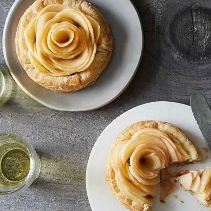 Apple rose tartlets on white plates on a table.