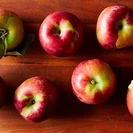 Red apples lined up on a wooden table.