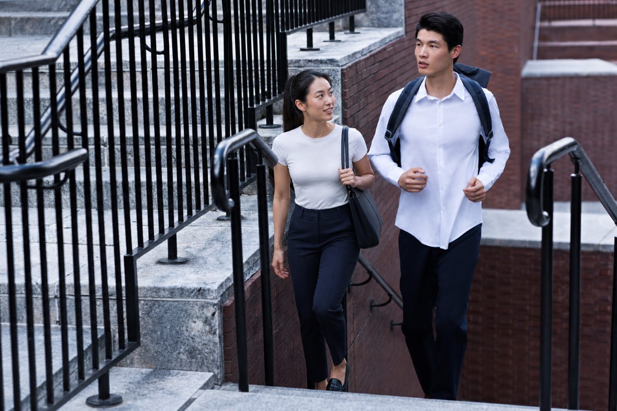 Man and woman in Ministry of Supply Kinetic Pants descending brick city stairs together, commute-ready