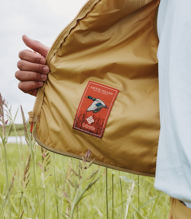 Close-up of a model opening their jacket to reveal an orange Sauvie Island patch with a duck on it.