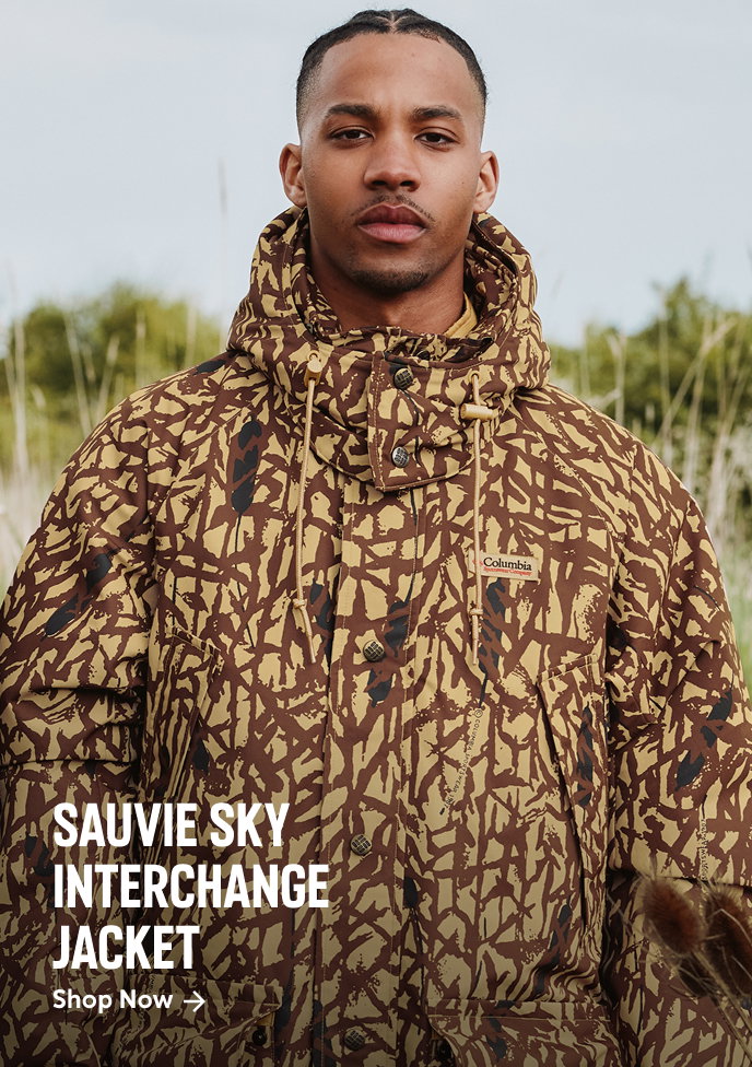 A man standing outside, wearing a camo jacket with text: SAUVIE SKY INTERCHANGE JACKET
