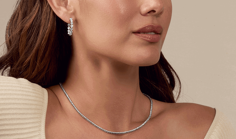 Model wearing luxurious diamond hoop earrings and a delicate white gold necklace.