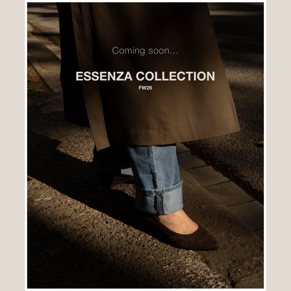 Close-up of a woman wearing brown pointed-toe shoes with cuffed jeans and a long coat, introducing Essenza FW26.