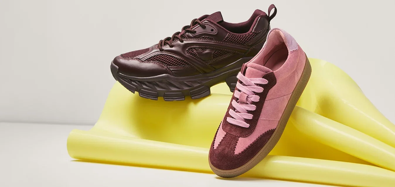 Een paar bordeauxrode en roze sneakers die rusten op een opgevouwde gele fitnessmat tegen een effen achtergrond.