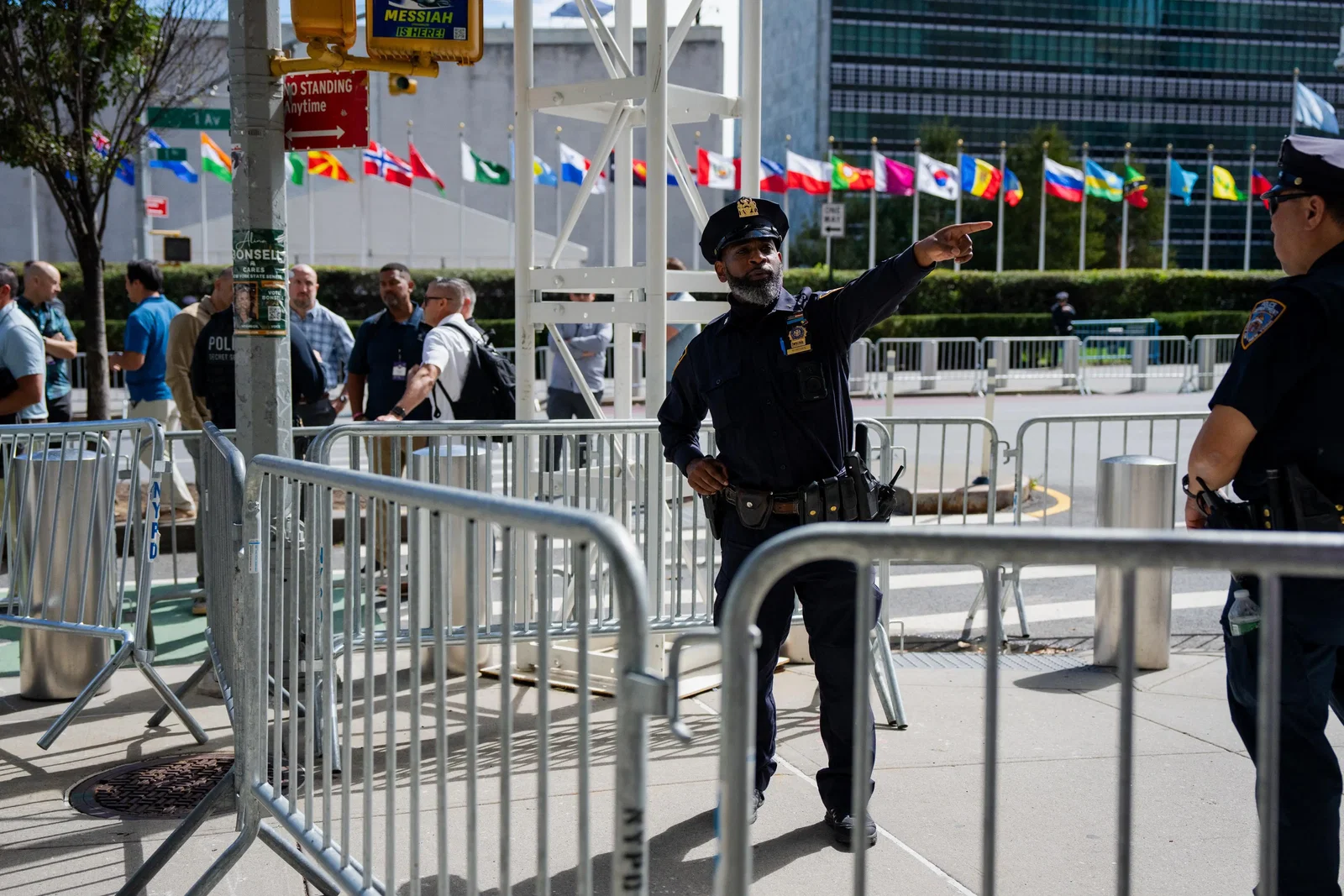 A police officer stands behind barricades outside the United Nations building in New York, pointing someone away. 