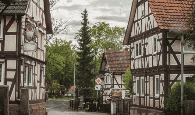 Narrow street lined with traditional half-timbered houses, lush greenery, and an overcast sky.