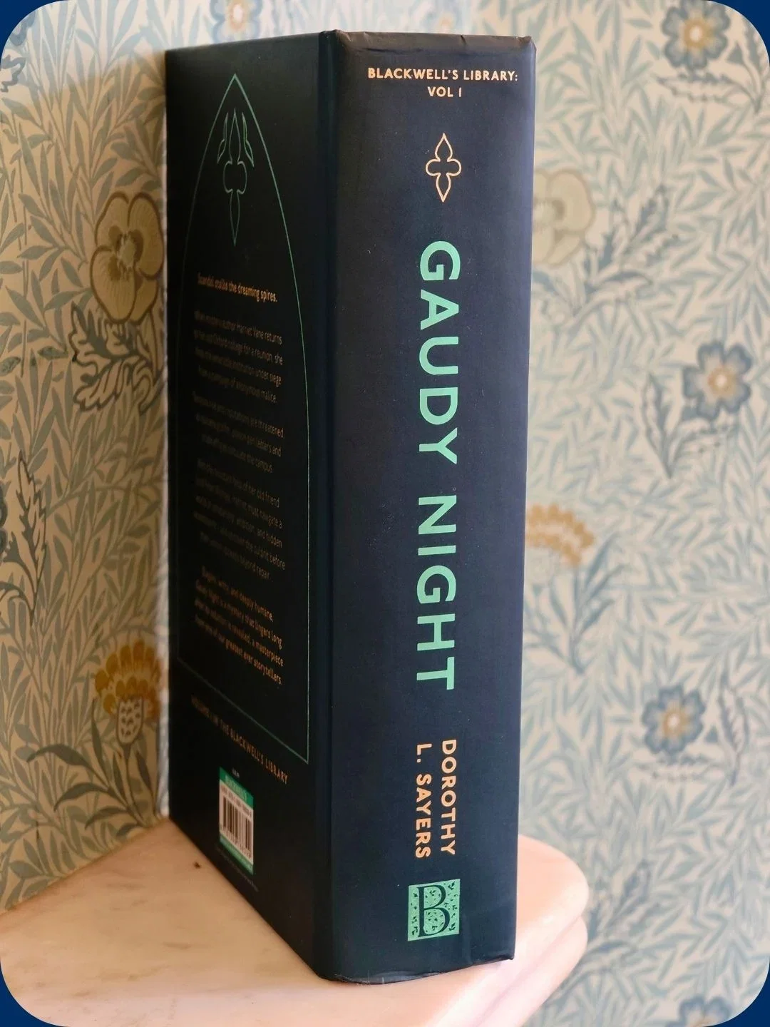 "Gaudy Night" book on floral wallpaper shelf.