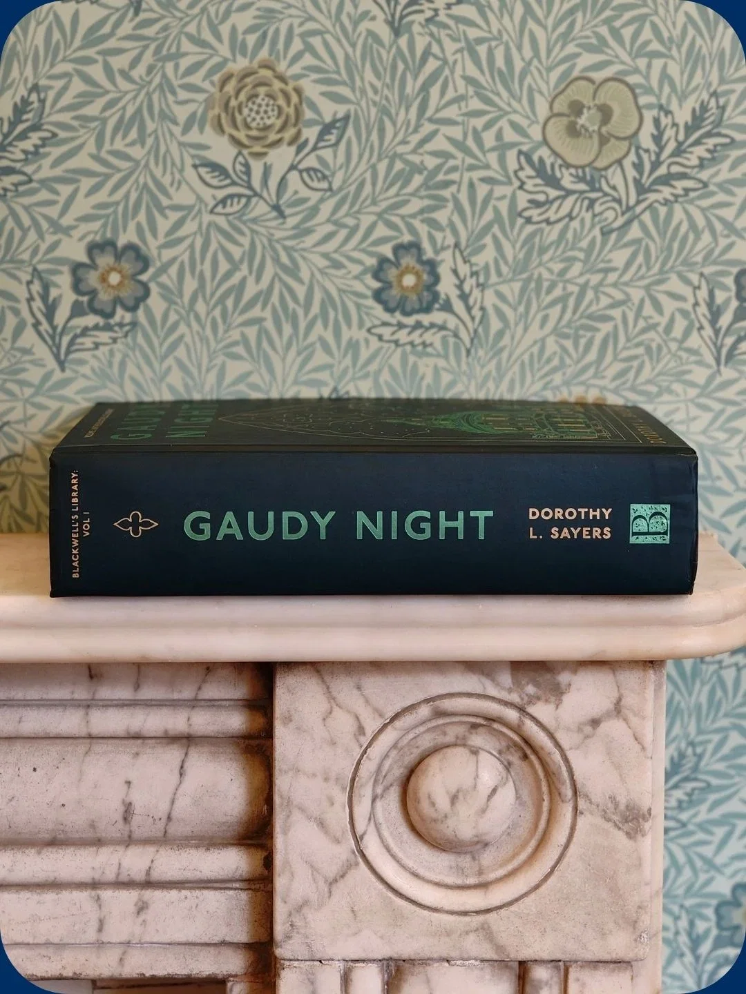 Book 'Gaudy Night' on marble shelf, floral wallpaper.