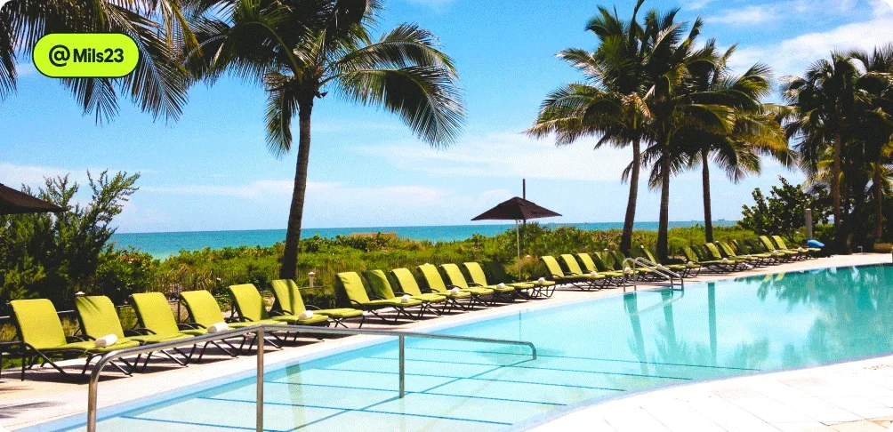 Image description: A row of beach chairs and a pool with palm trees and the ocean in the background, photo taken by @Mils23