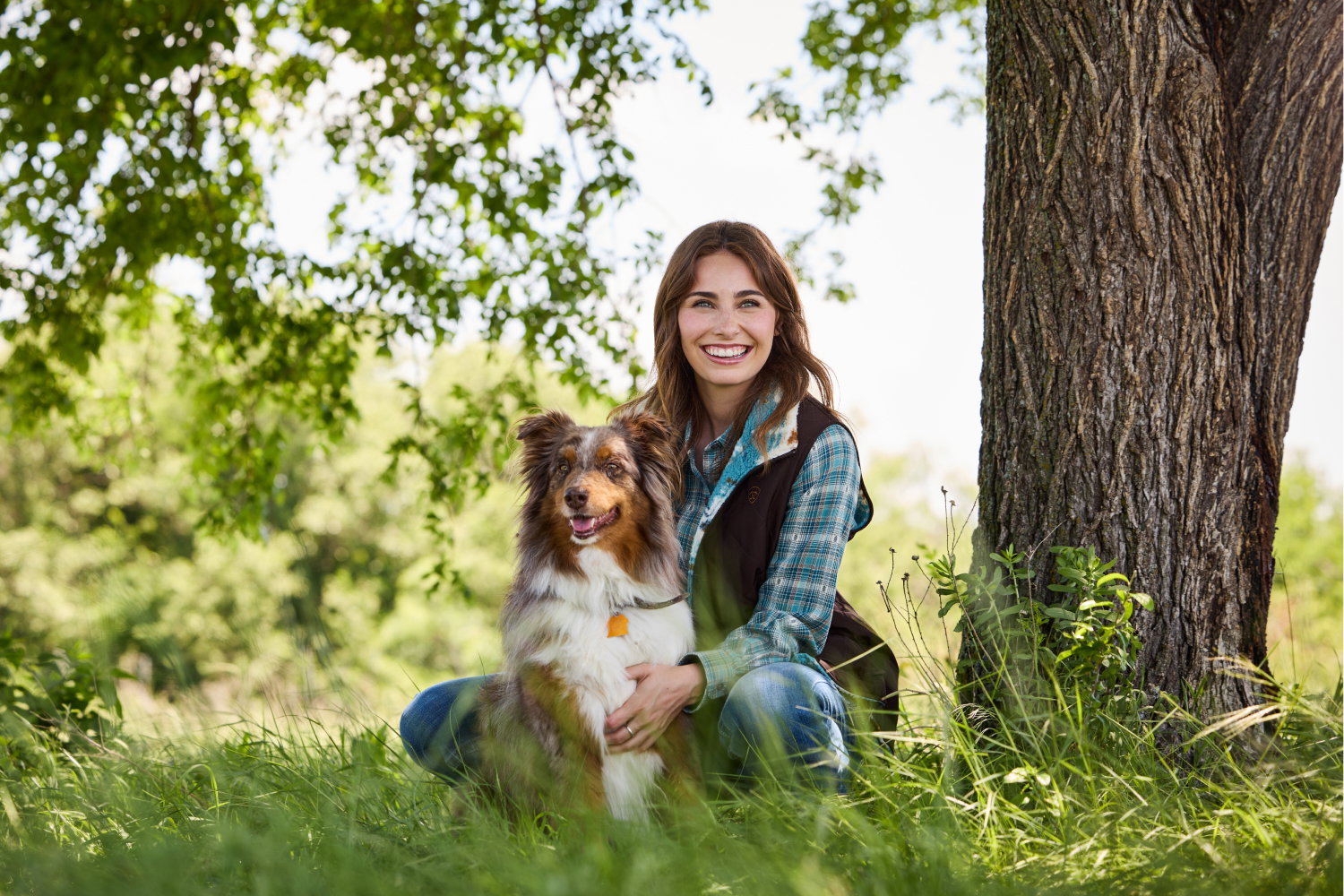 Women with her dog sitting by tree.