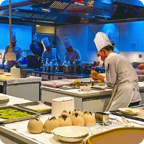 Image Description: Kitchen at a fine dining restaurant with multiple chefs in white chef’s coats and hats at various stations.