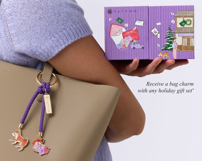 An image of a model showcasing Tatcha's holiday bag charm complimentary with every holiday gift set 